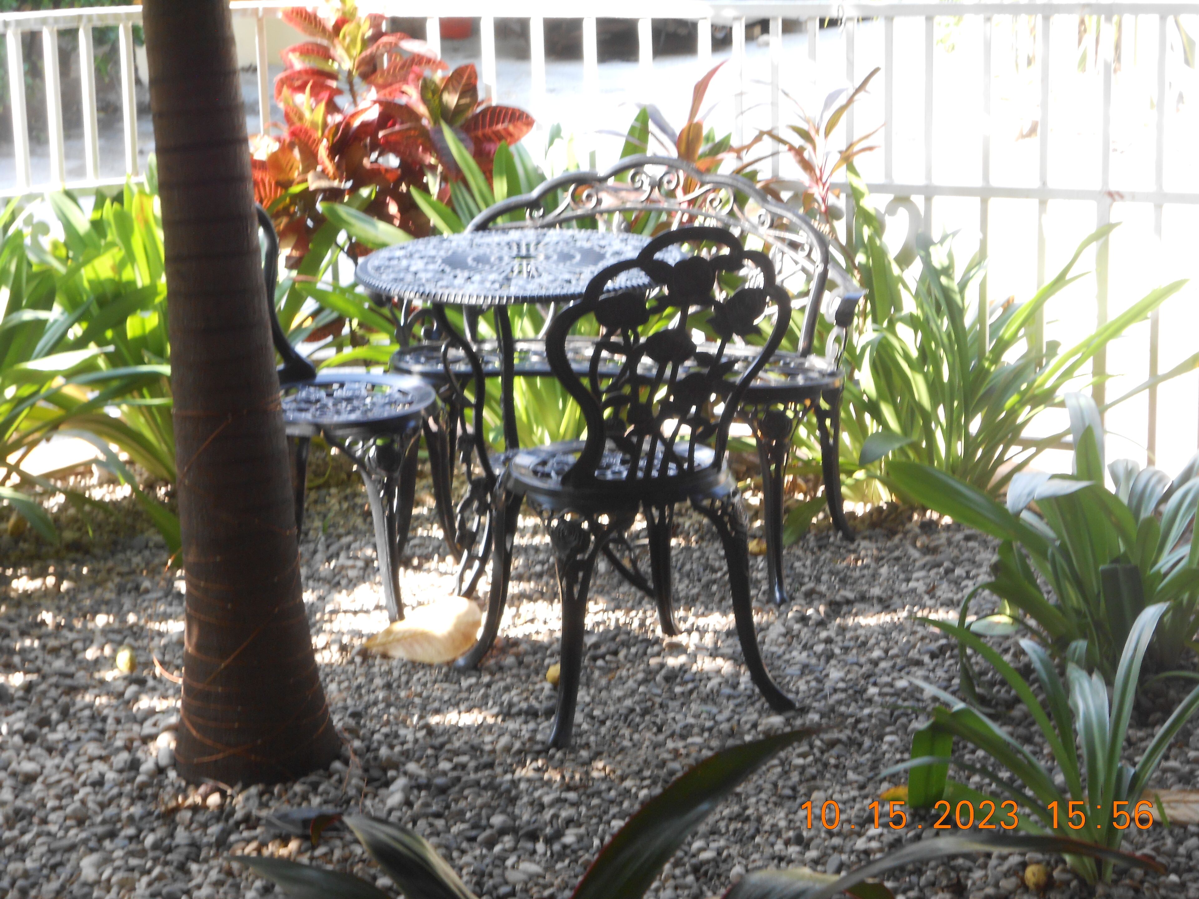 An outdoor seating area with metal tables and chairs, surrounded by gravel and various plants.