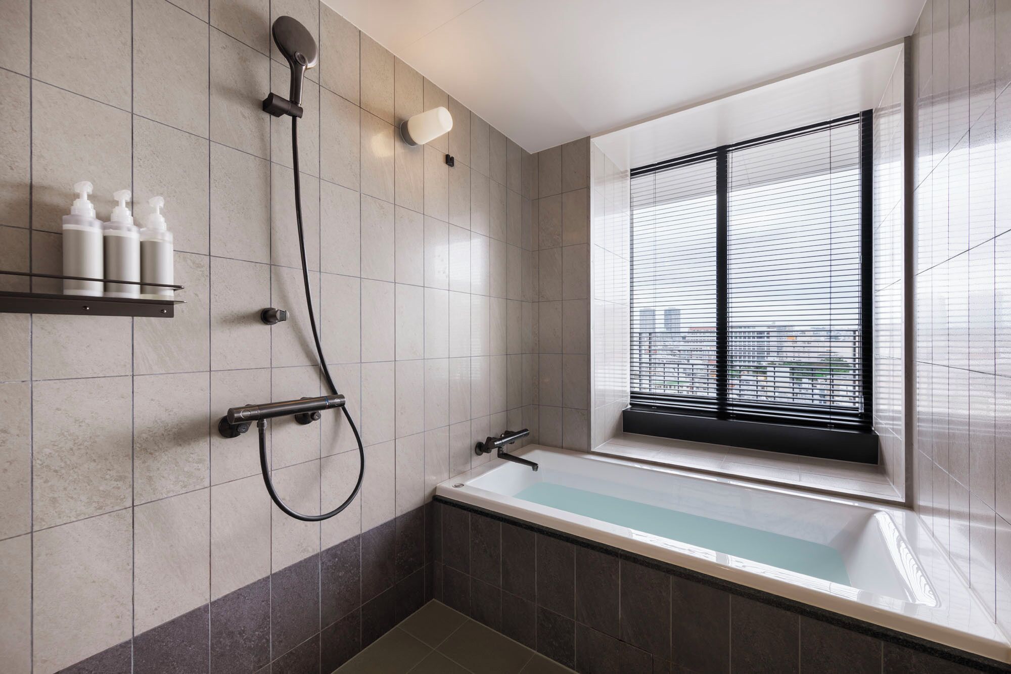 A modern bathroom with a bathtub, a shower, and a window with blinds.