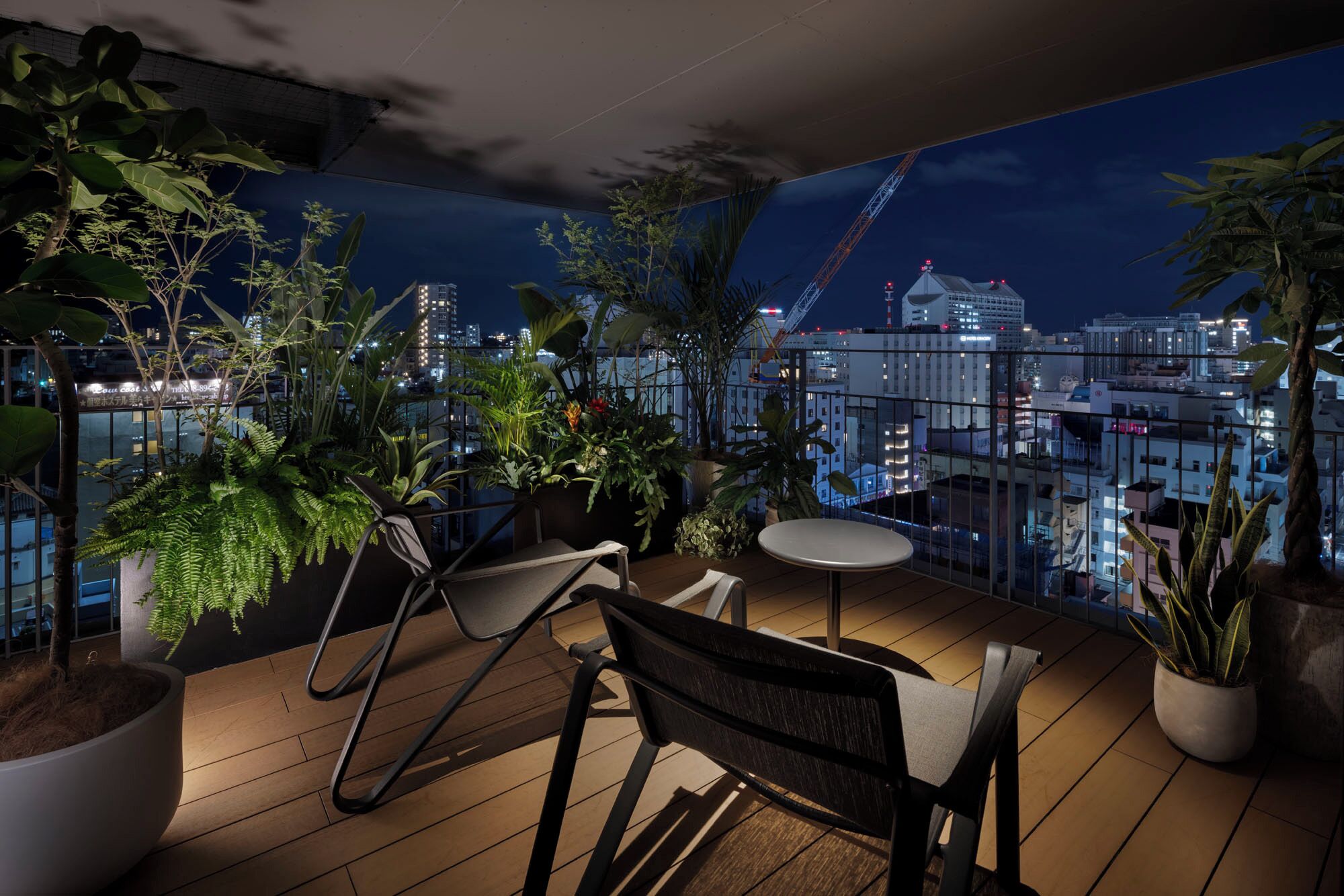 Ein Balkon mit Holzboden, zwei Stühlen, einem kleinen runden Tisch und Blumentöpfen.
