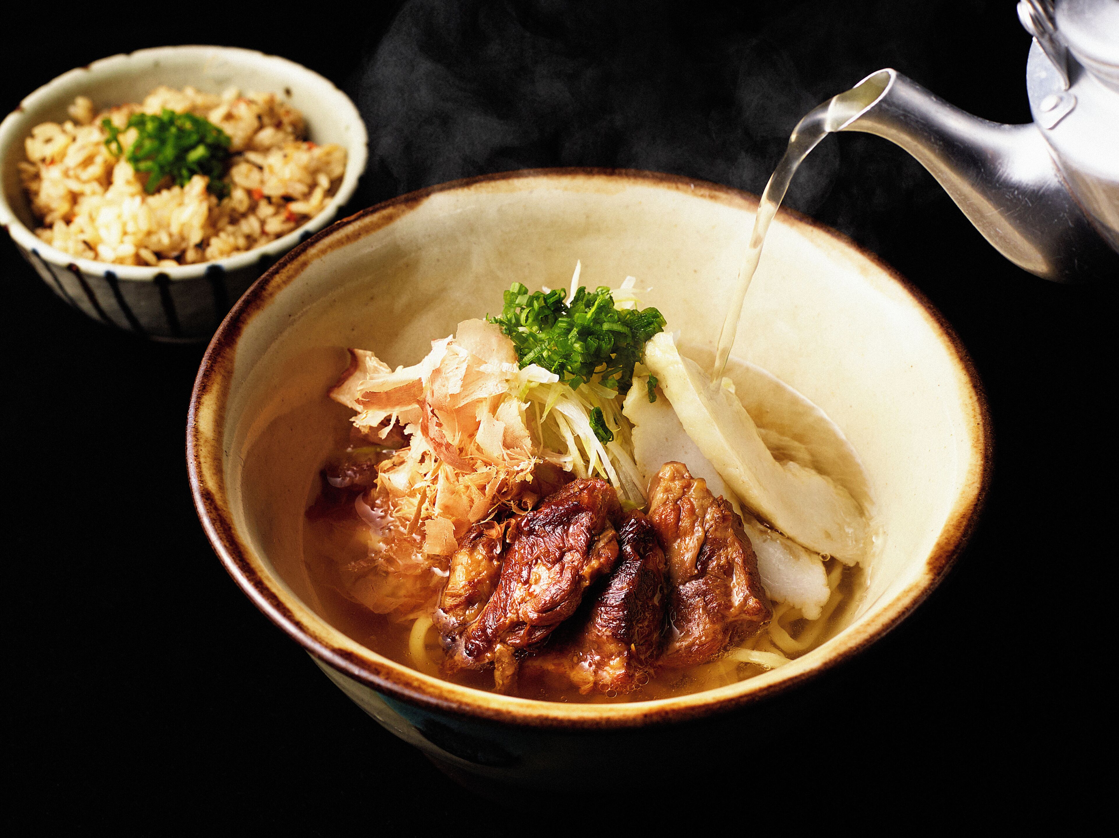 A bowl of soup with meat and vegetables, a small bowl of rice, and a teapot.