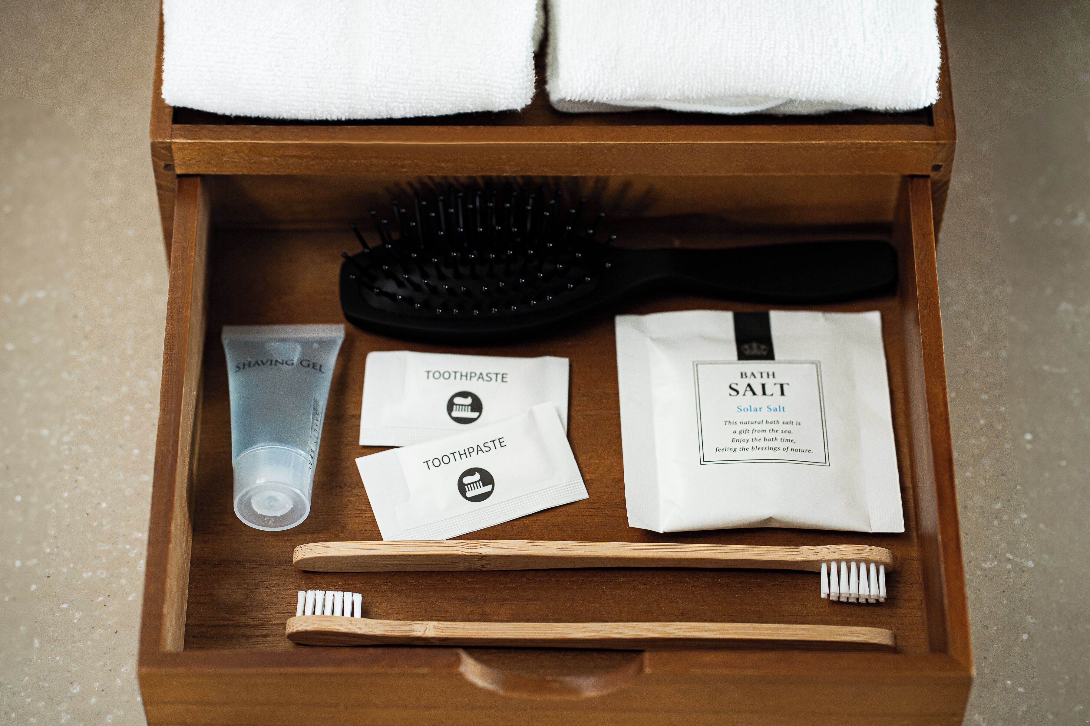 A wooden drawer containing a toothbrush, toothpaste, a hairbrush, and a bag of bath salt.