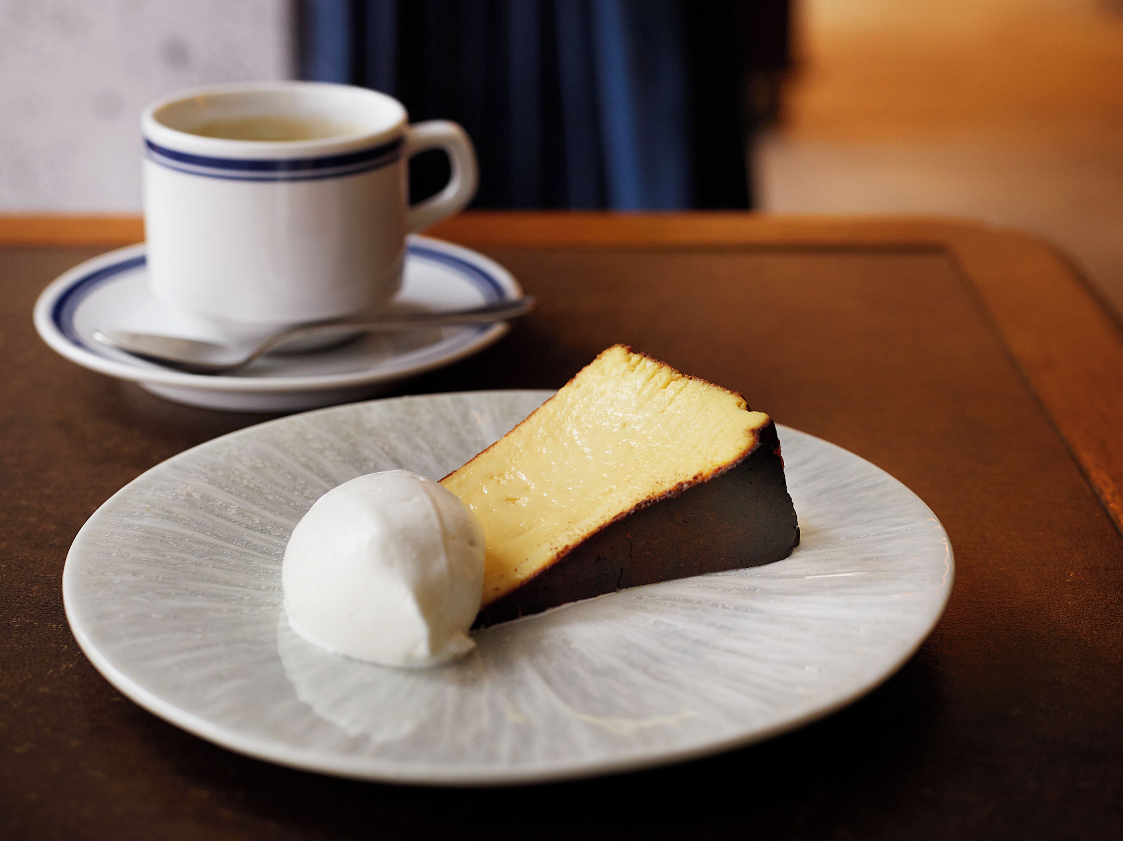 Ein Dessertteller mit einem Stück Käsekuchen und einer Kugel Eis auf einem Tisch.