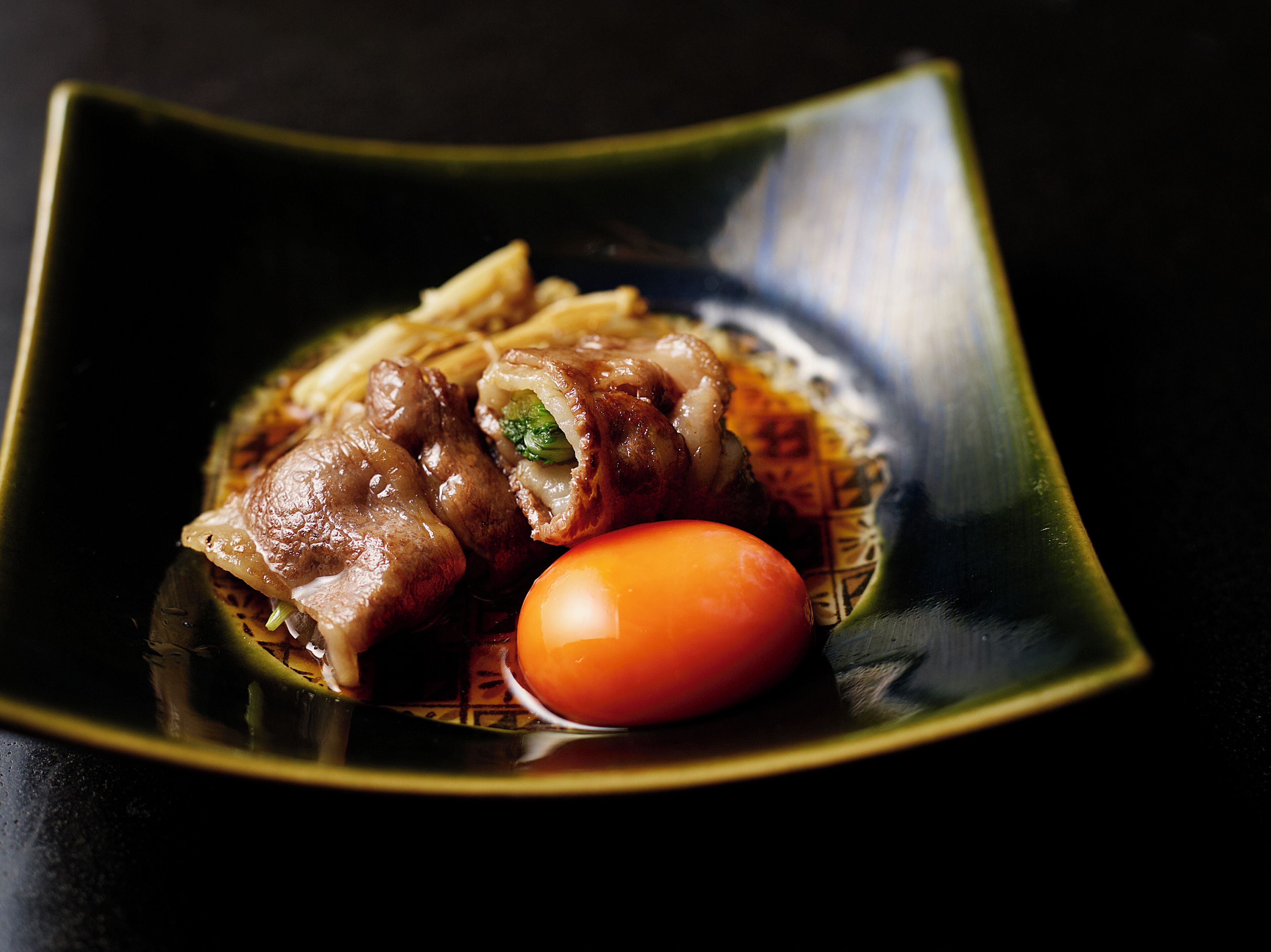 A dish with meat and vegetables on a dark plate.