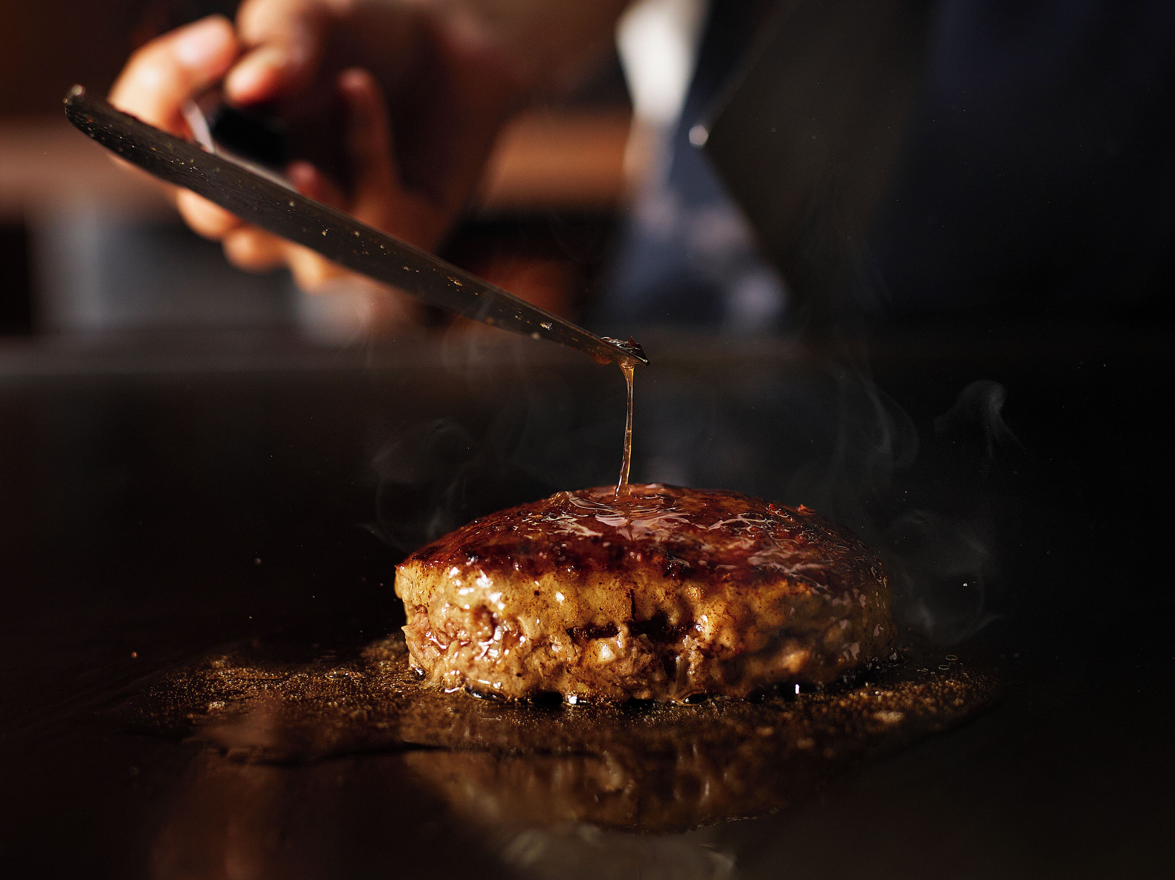 A close-up of a steak being sliced with a knife, with visible juices and steam.