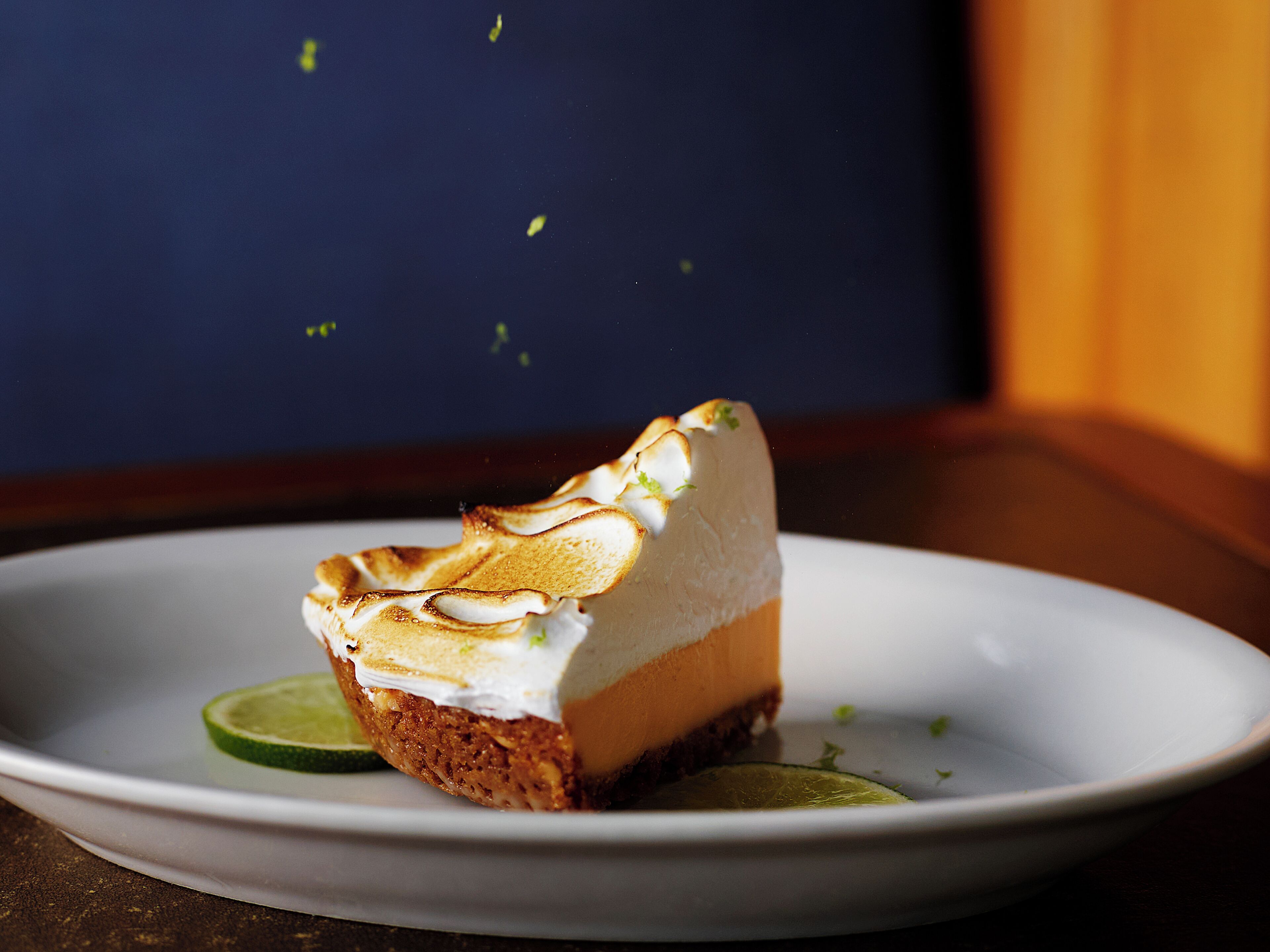 A slice of cheesecake with a meringue topping on a white plate, garnished with a lime slice.