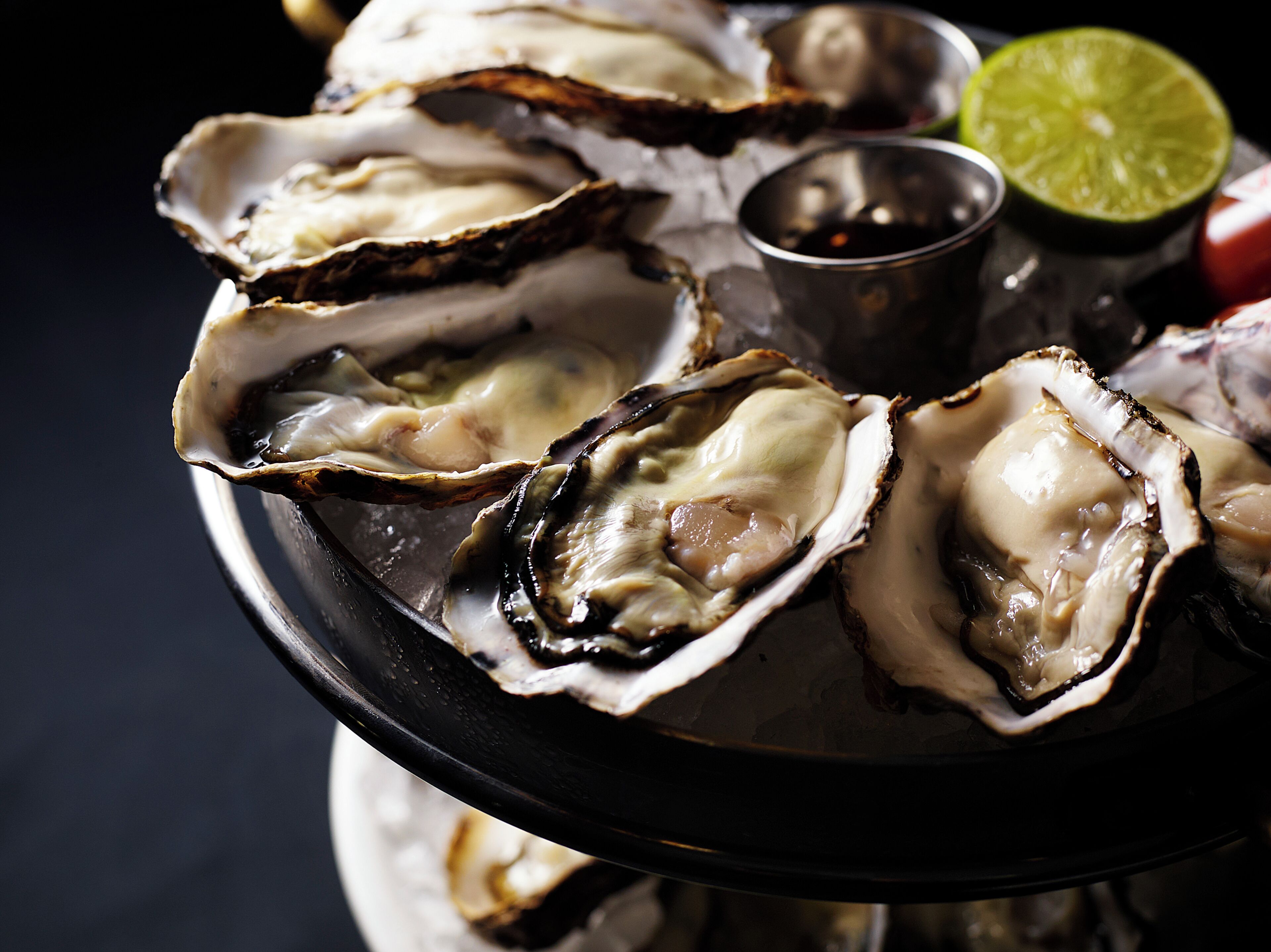 A tray of oysters with a lime wedge and a small bowl of sauce.