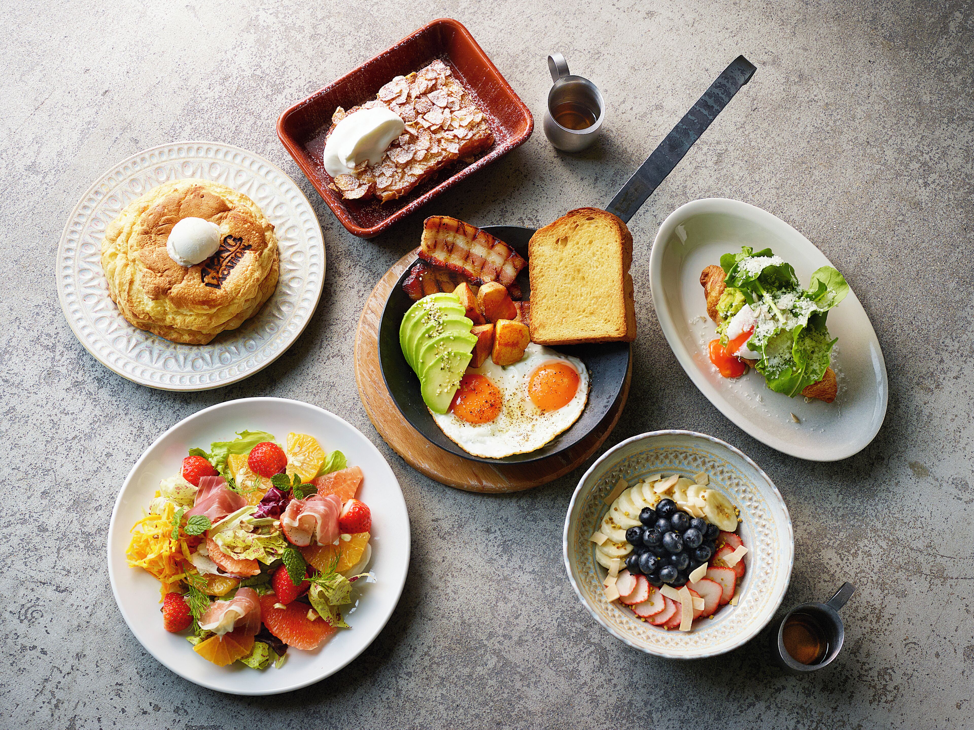 Ein Frühstückstisch mit verschiedenen Speisen, darunter Pfannkuchen, Toast, Eier und Obstsalat.