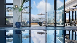 A modern indoor pool area with glass walls, a clear view of the sky, and outdoor seating. - Southwest Grand Hotel (Naha)