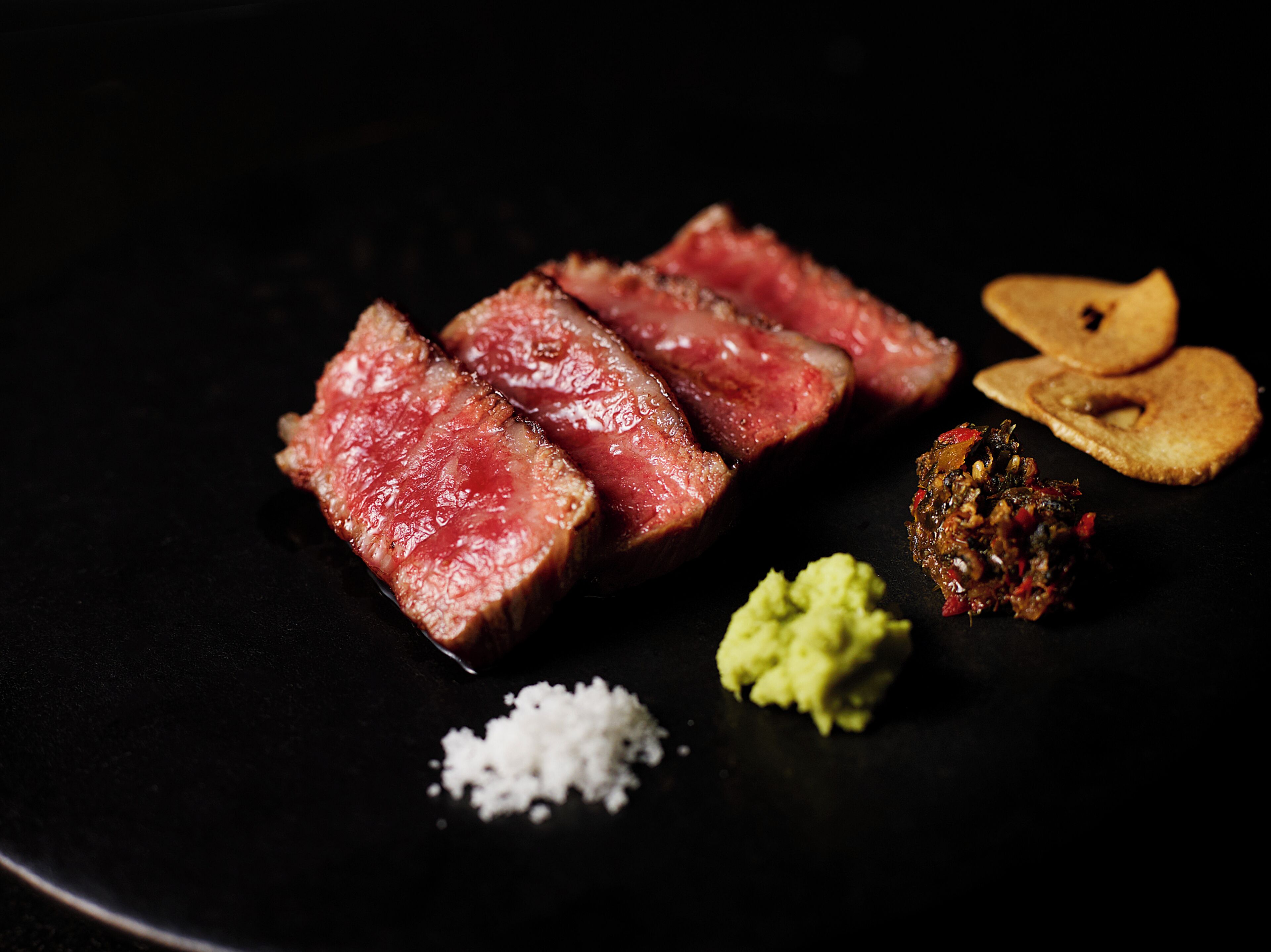 A plate with sliced steak, guacamole, and a spice mix.
