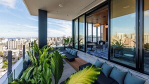A modern balcony with a city view, seating area, and large windows. - Southwest Grand Hotel (Naha)