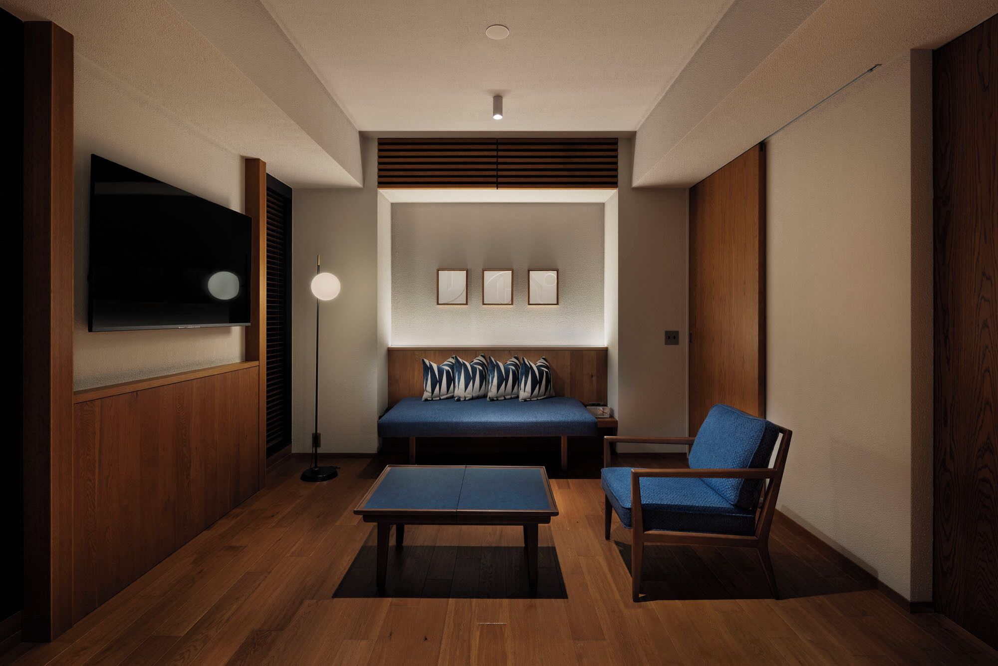 Una sala de estar moderna con un sofá, un sillón, una mesa de centro y un televisor de pantalla plana montado en la pared.