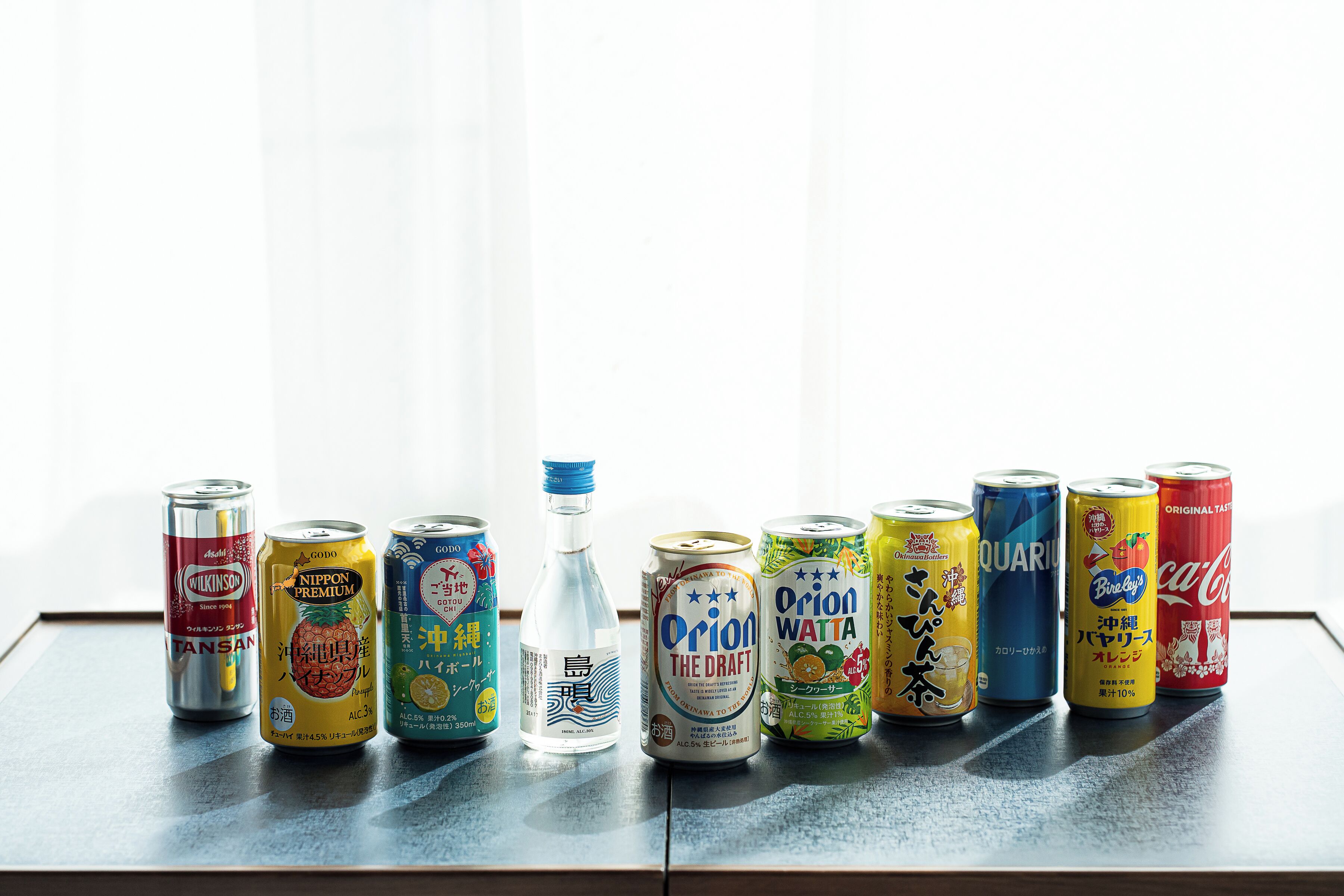 Una fila de latas de bebidas y una botella sobre una mesa.