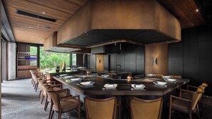 A modern restaurant with a central island, wooden chairs, and a large overhead ventilation system. - Southwest Grand Hotel (Naha)