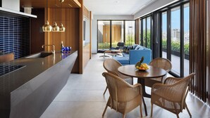 A modern kitchen with a central island, a dining area with wicker chairs, and a large window offering a city view. - Southwest Grand Hotel (Naha)