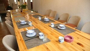 A long wooden dining table with blue and white patterned plates, clear glasses, and a pink ashtray. - Yichun Jingfu Courtyard · Linmei Aishe Homestay (Yichun)