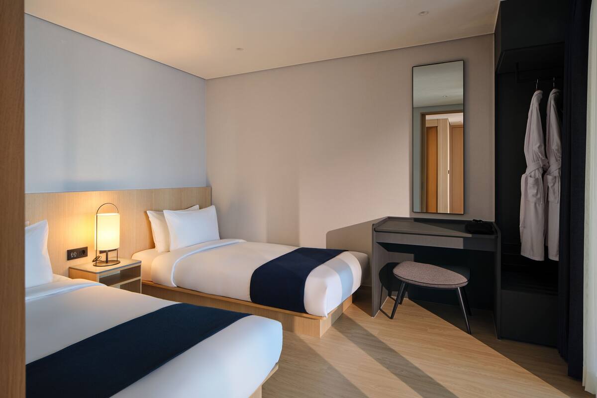 Habitación de hotel con dos camas, un escritorio, una silla, una bata y un espejo.