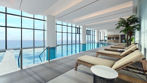 A modern indoor pool area with lounge chairs and a view of the ocean.