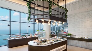 A modern reception area with a buffet counter, large windows offering ocean views, and a decorative metal structure with hanging lights.