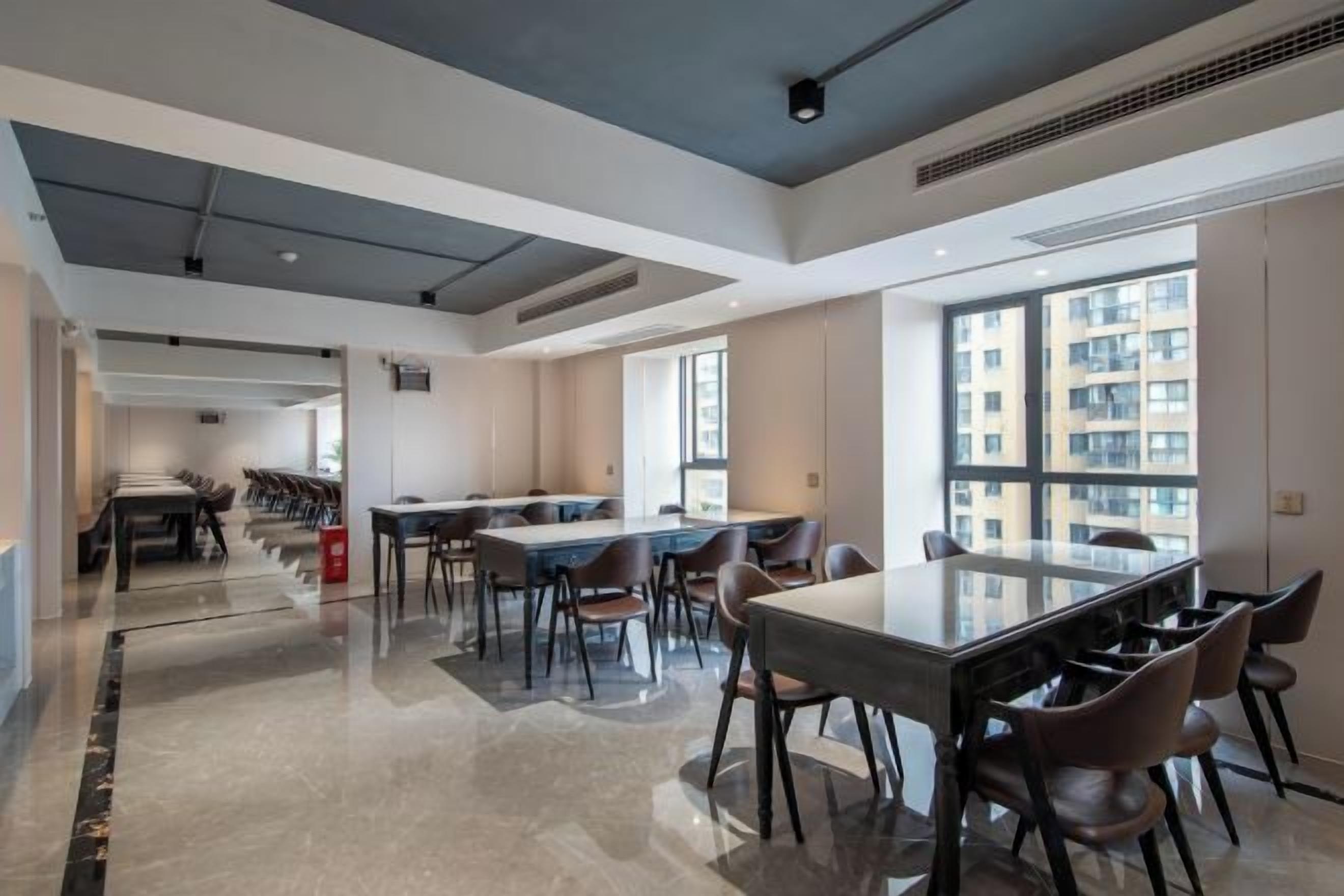 Un comedor moderno de hotel con una larga mesa, sillas y vistas de la ciudad a través de amplias ventanas.