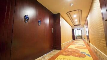 A hotel corridor with wooden walls, a patterned carpet, and a door with a number plate.