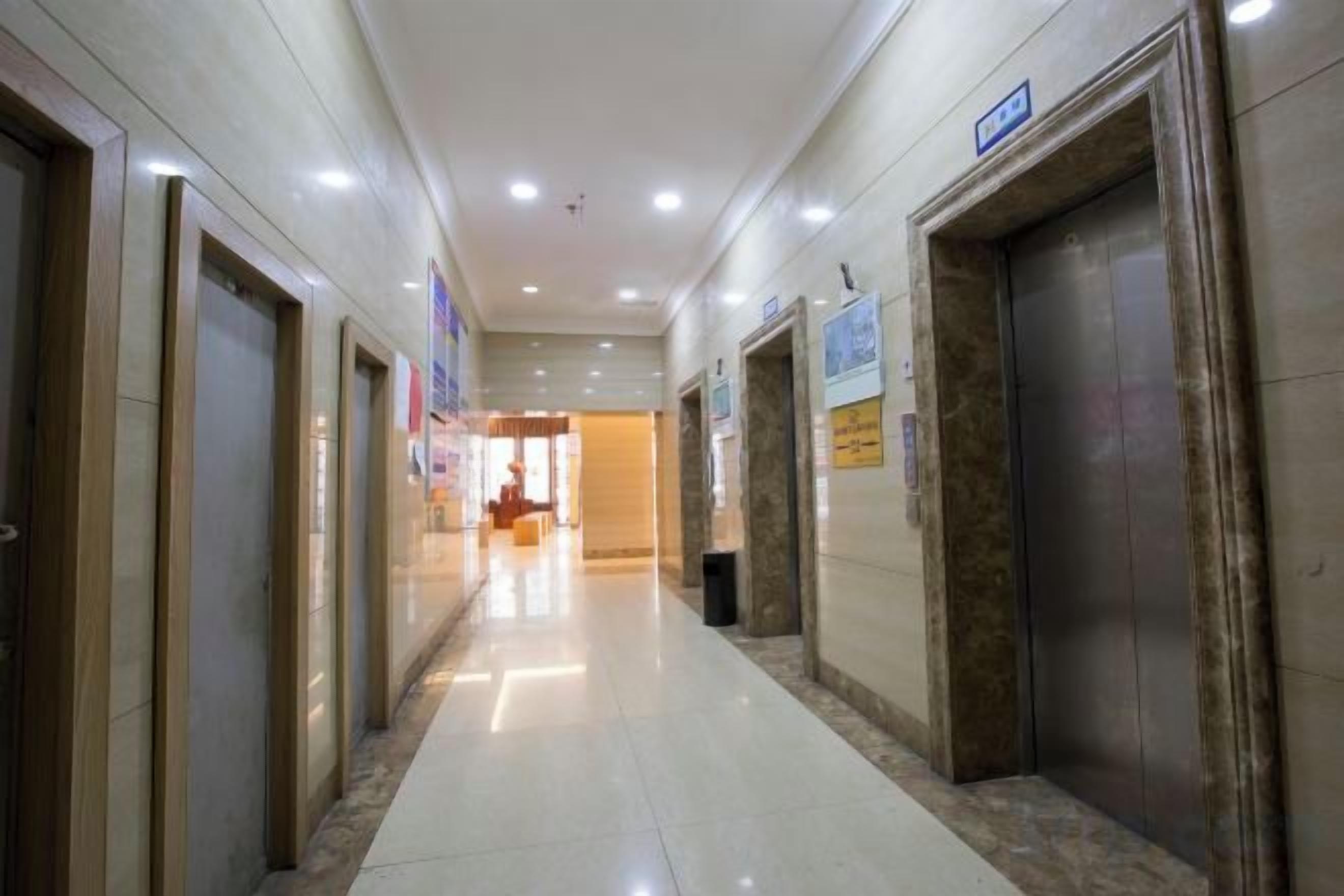 A corridor with doors on either side, leading to elevators and a reception area in the distance.