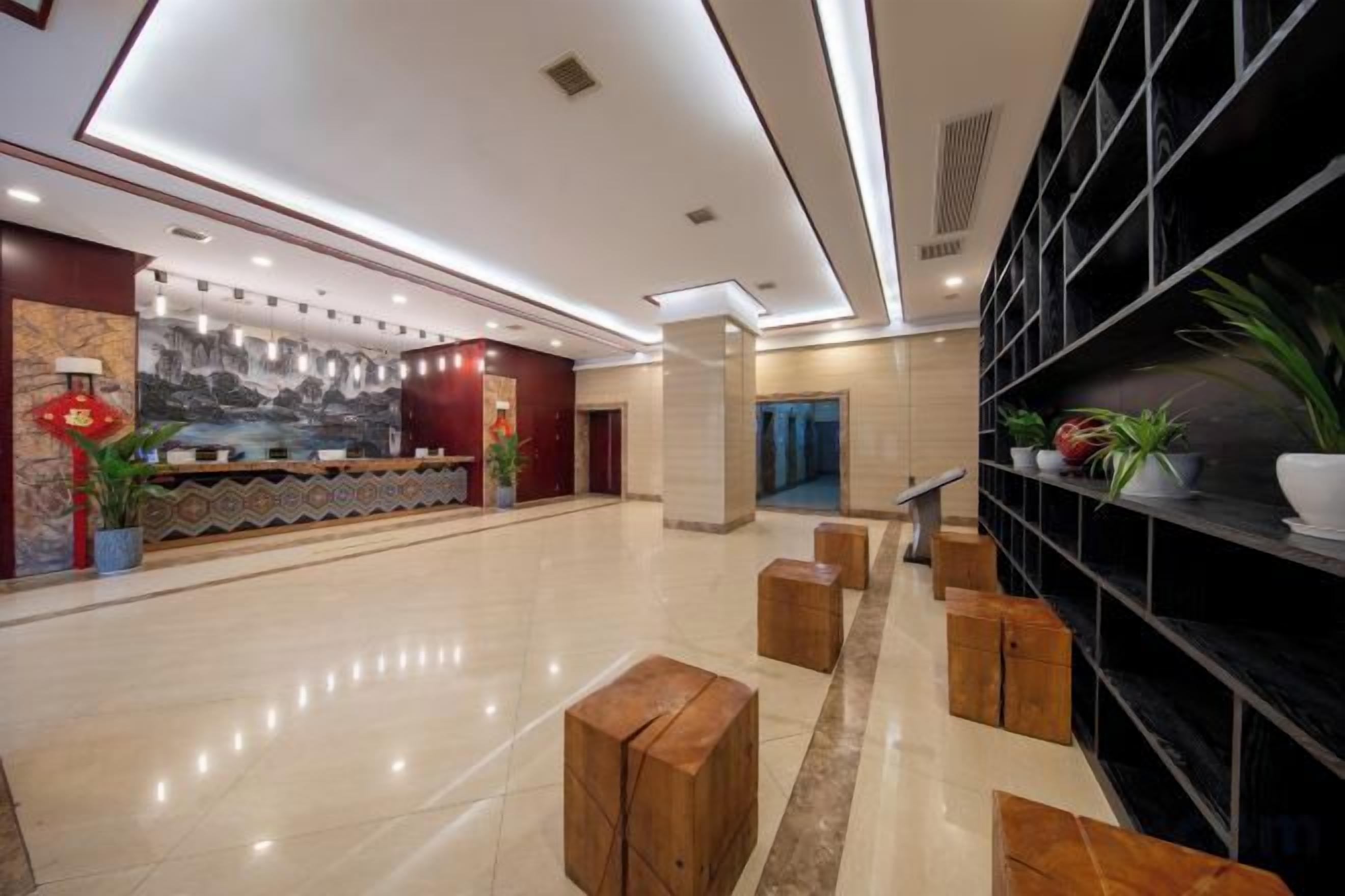 A hotel lobby with a reception desk, seating area, and a wall with shelves.