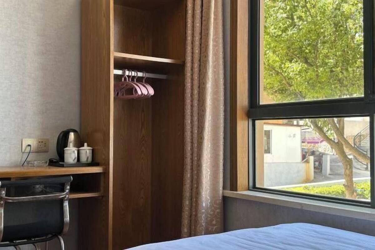 Hotelkamer met een houten bureau, een stoel, een bed, een raam met uitzicht op bomen en een kledingkast met kledingroede.