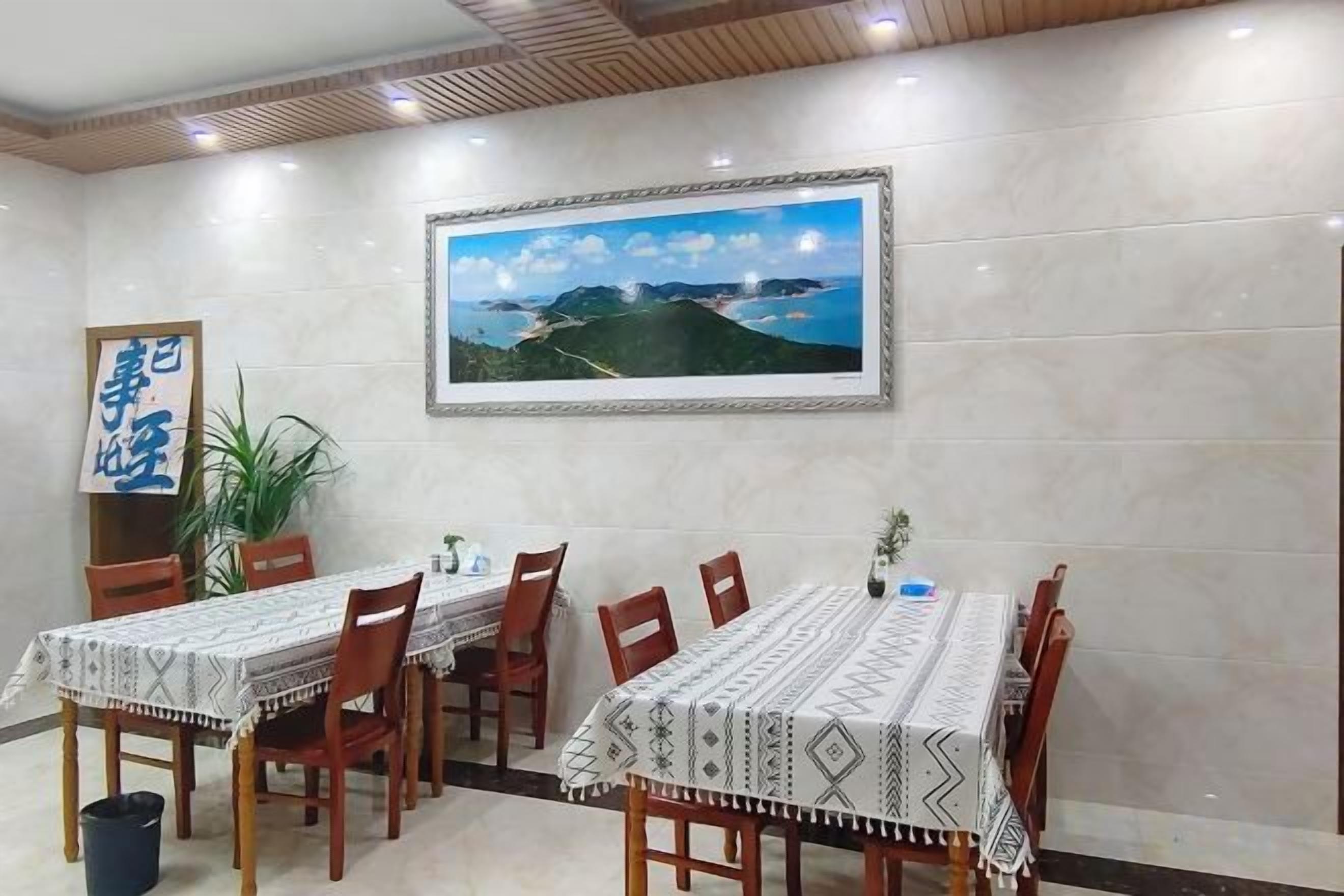 A dining area with a long table, chairs, and a framed landscape painting on the wall.