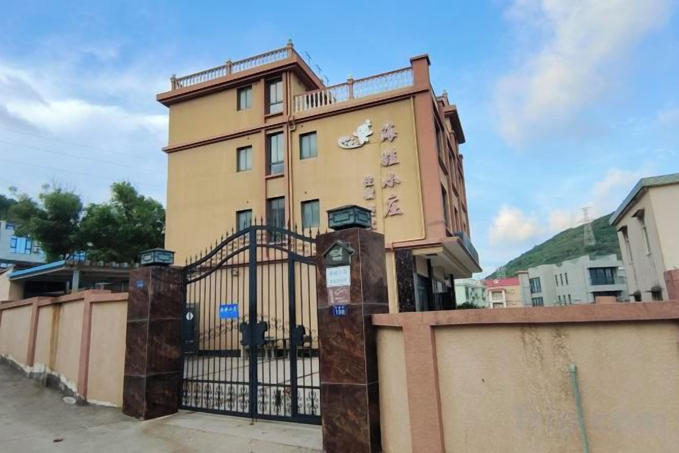 A multi-story building with a gated entrance, a sign with Chinese characters, and a clear sky.