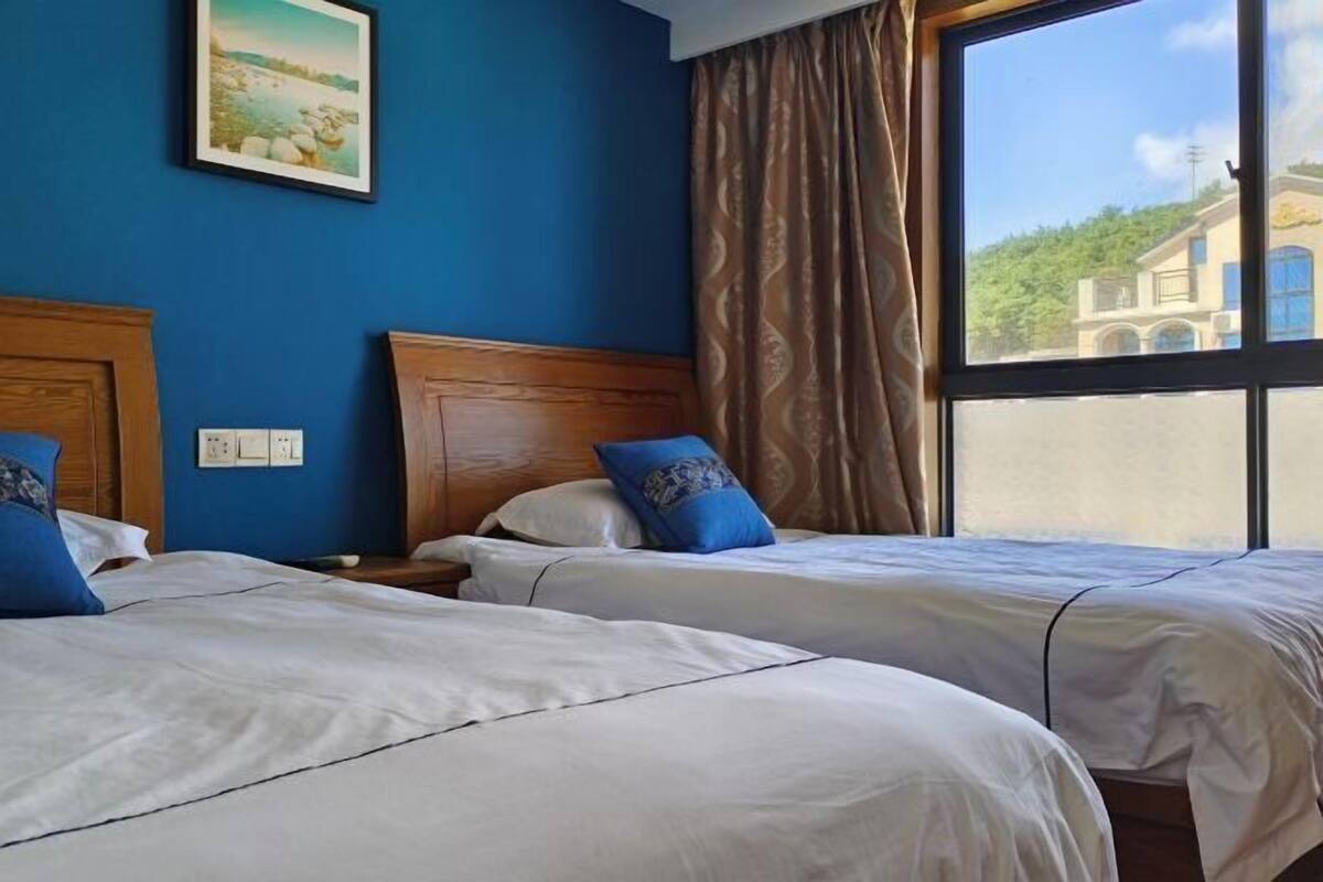 Een hotelkamer met twee bedden, een groot raam met uitzicht op een gebouw, en een schilderij aan de muur.