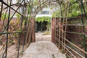 A concrete pathway leading through a brick wall with a metal trellis structure on either side. - Shenmi Sidou Hostel (Nanjing)