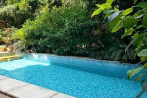A swimming pool surrounded by lush greenery. - Shenmi Sidou Hostel (Nanjing)
