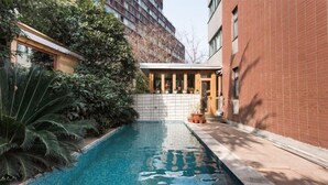 A swimming pool with tiled edges, surrounded by greenery and a brick building. - Shenmi Sidou Hostel (Nanjing)