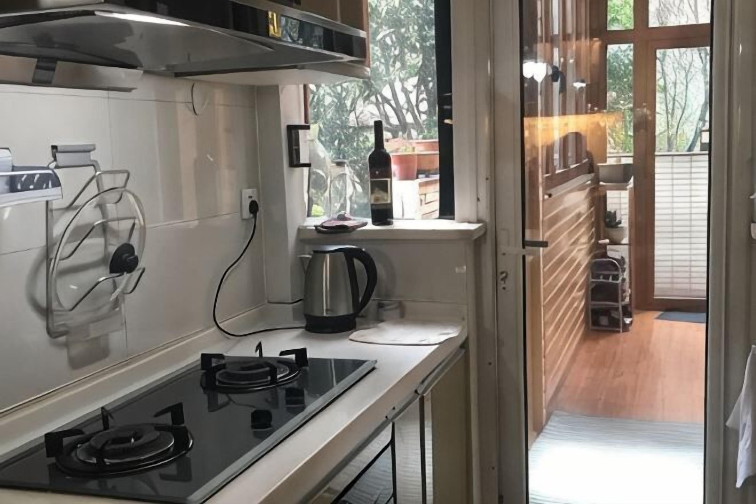 A kitchen with a stove, kettle, and window overlooking a wooden deck.