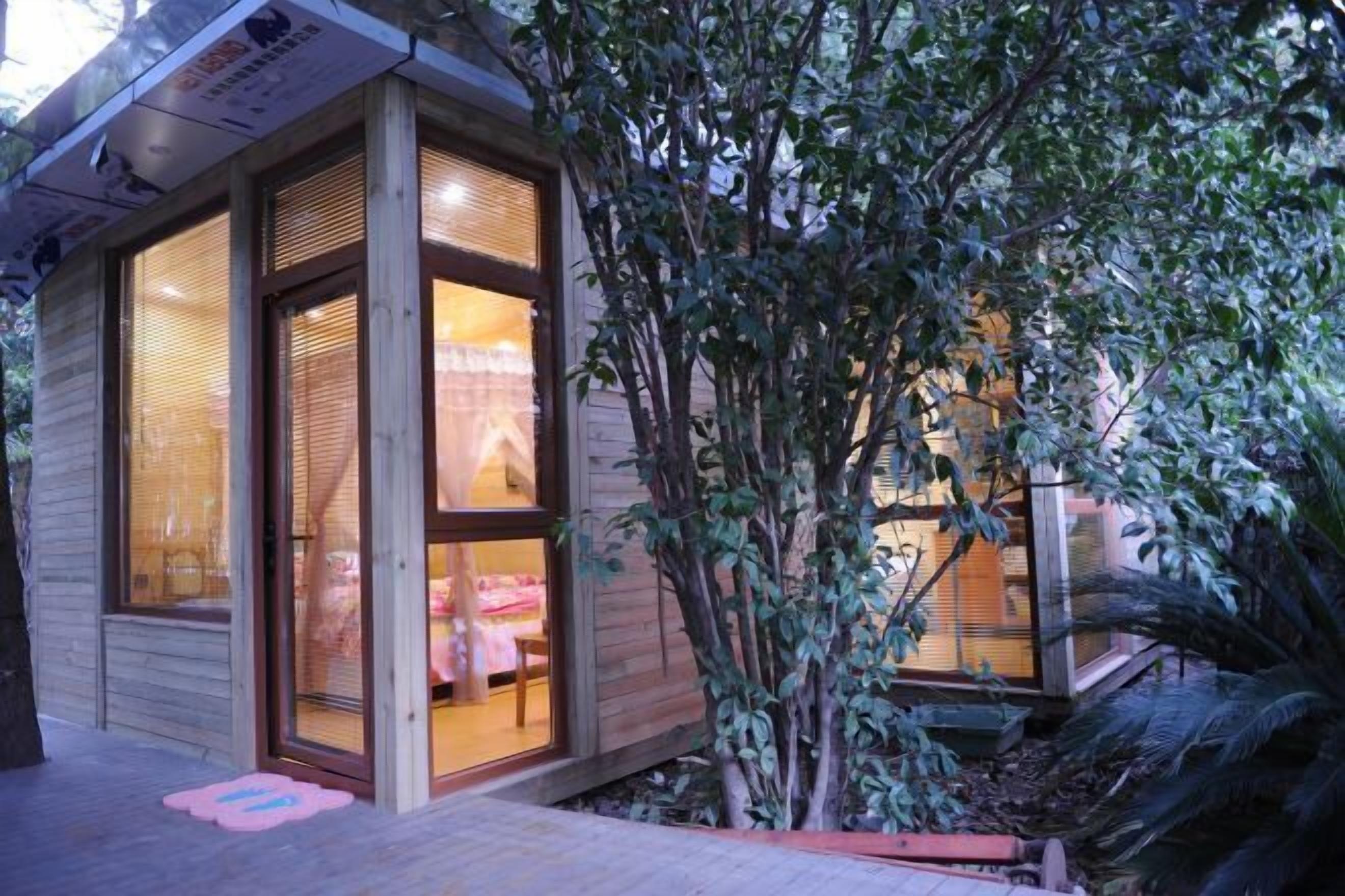 Une cabane en bois dotée de grandes fenêtres et dont l’intérieur est visible, avec un lit et une table.