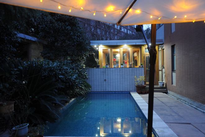 A swimming pool with a tiled deck, surrounded by potted plants and a covered area with string lights.