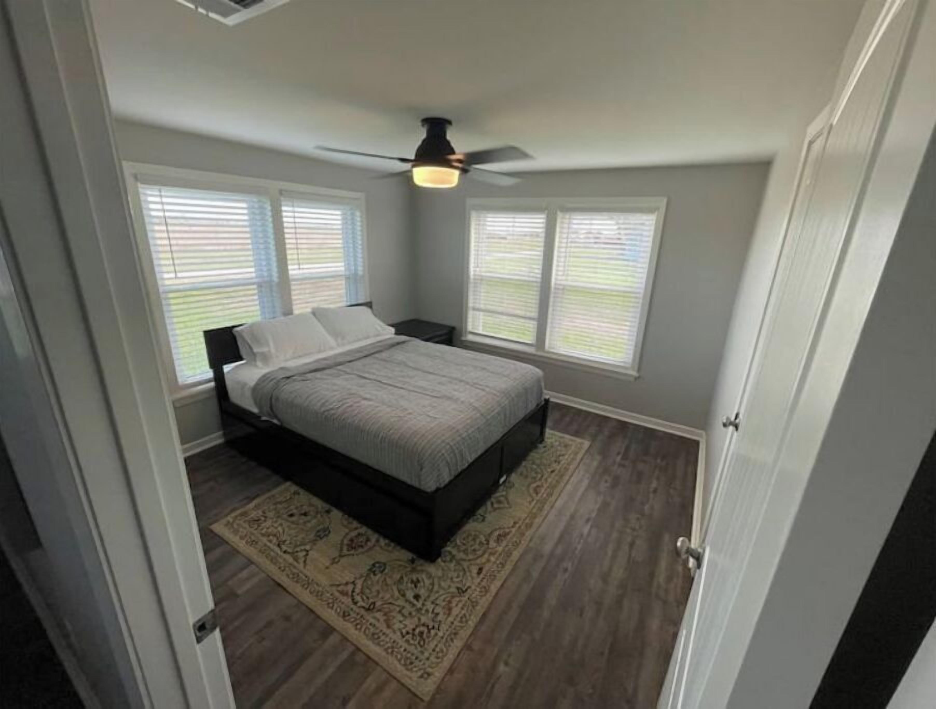 A bedroom with a bed, a ceiling fan, and two windows with blinds.