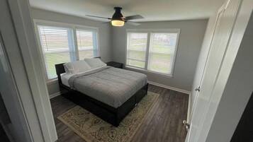 A bedroom with a bed, a ceiling fan, and two windows with blinds.