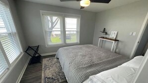 A bedroom with a bed, a ceiling fan, a window, a small table, and a rug.