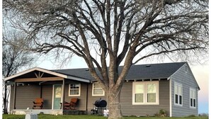 A single-story house with a covered porch, a large tree in front, and a lawn.