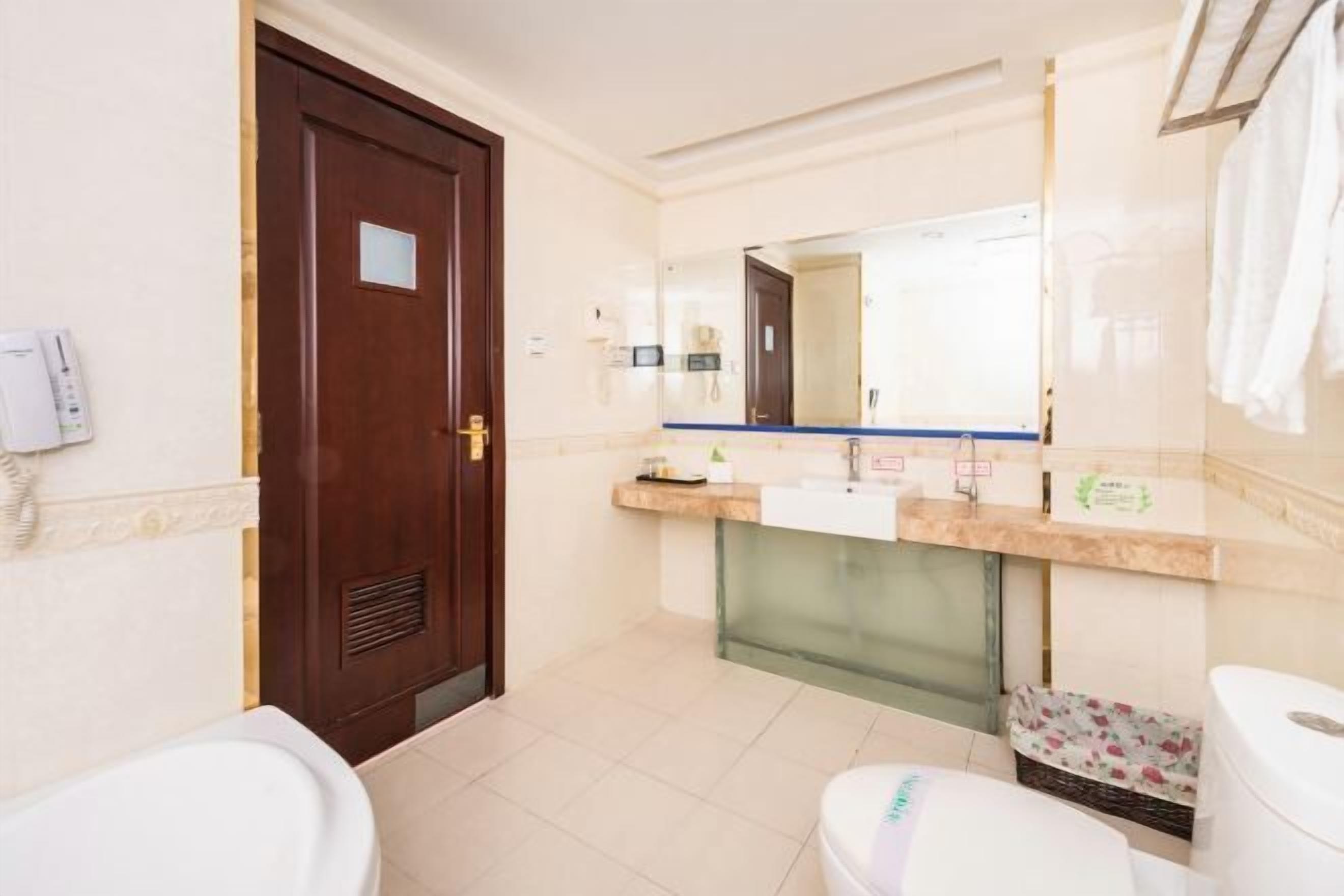 Casa de banho com porta de madeira, sanita branca, lavatório com espelho e barra de toalhas.