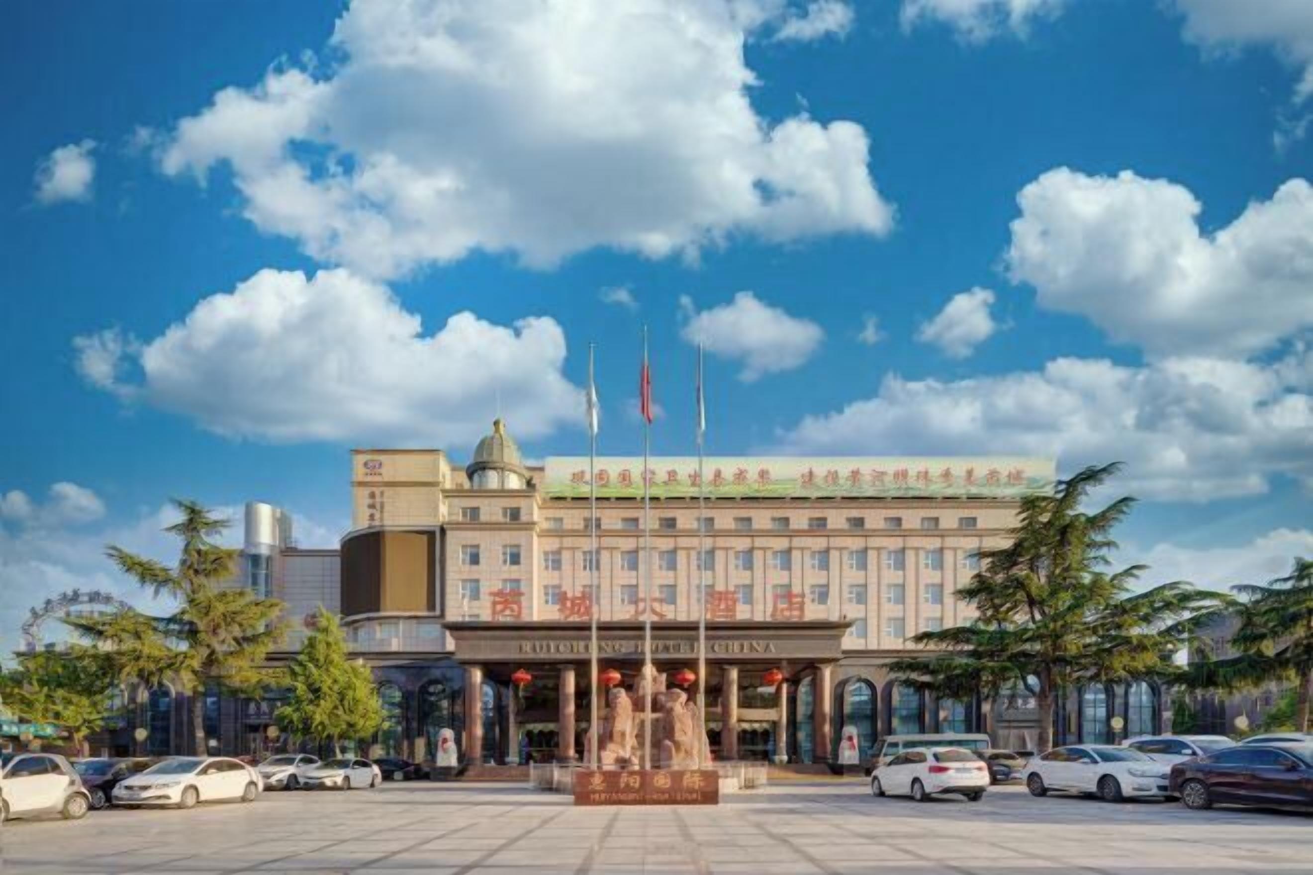 A hotel with a prominent entrance, multiple flags, and a parking lot with cars.