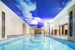 Piscina com teto que simula um céu com nuvens, cercada por paredes com acabamento texturizado.