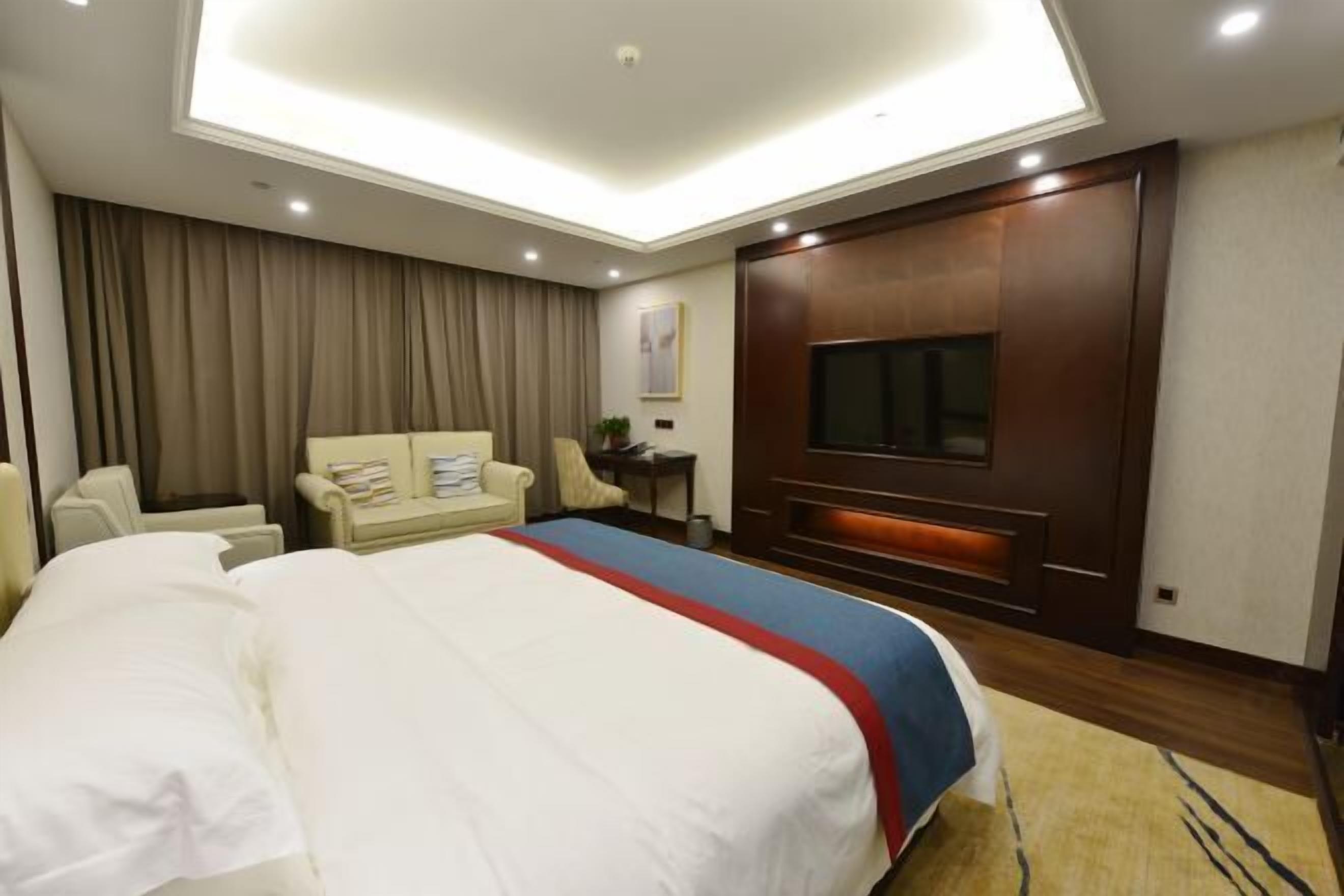 A hotel room with a large bed, a desk, a chair, a television, and a ceiling light.