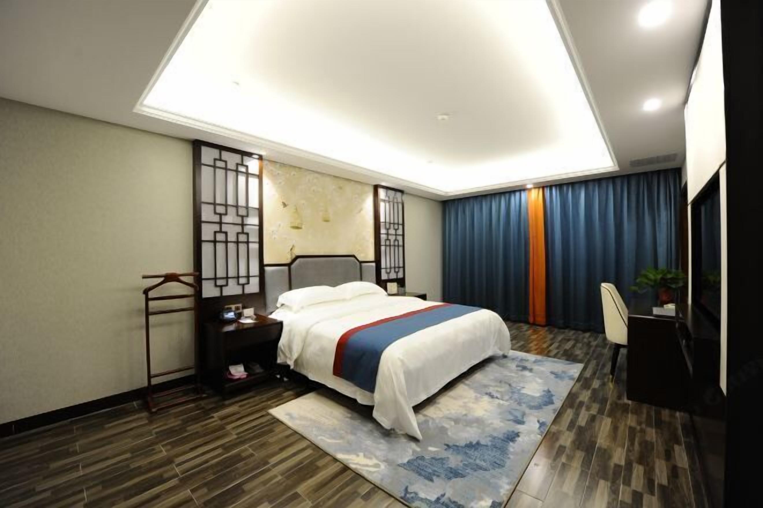 A modern hotel room with a large bed, a desk, a chair, and a desk lamp.