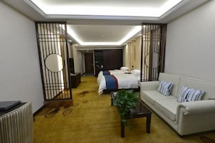 Una habitación de hotel con cama, sofá, mesa de centro y una planta.