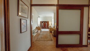 A hallway with wooden flooring, a rug, framed pictures on the wall, and a sliding door leading to a room with a bed and a nightstand. - Grand Botanic Garden Apartment by Vacationy (Porto)