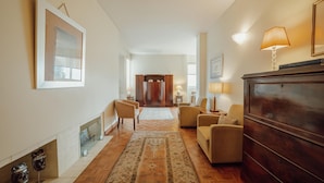 A spacious living room with a fireplace, a wooden floor, and a large rug. There are two armchairs and a sofa. - Grand Botanic Garden Apartment by Vacationy (Porto)