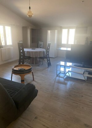 Un vaste espace de vie doté d’un plancher en bois, d’une table à manger et d’un téléviseur.