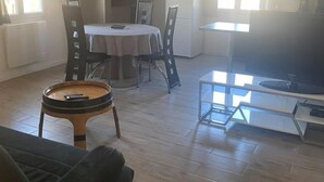 A spacious living area with a wooden floor, a round coffee table, a sofa, a dining table with chairs, and a television on a stand. - T1 in Blaye (Blaye)